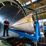 Photograph - manufacturing photo of aircraft nose cone being lifted into large industrial autoclave