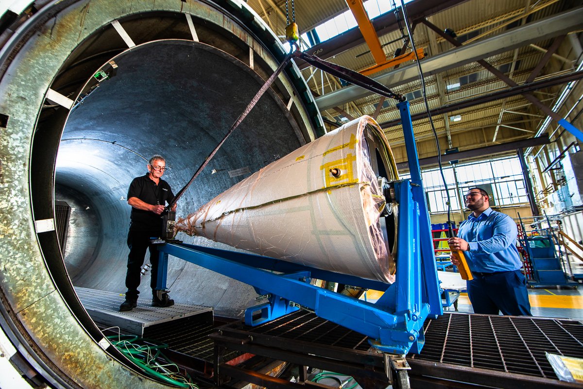 Photograph - manufacturing photo of aircraft nose cone being lifted into large industrial autoclave