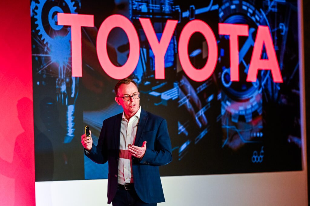 Speaker portrait of Nick Duckworth, CEO of Toyota MHUK with large Toyota display behind