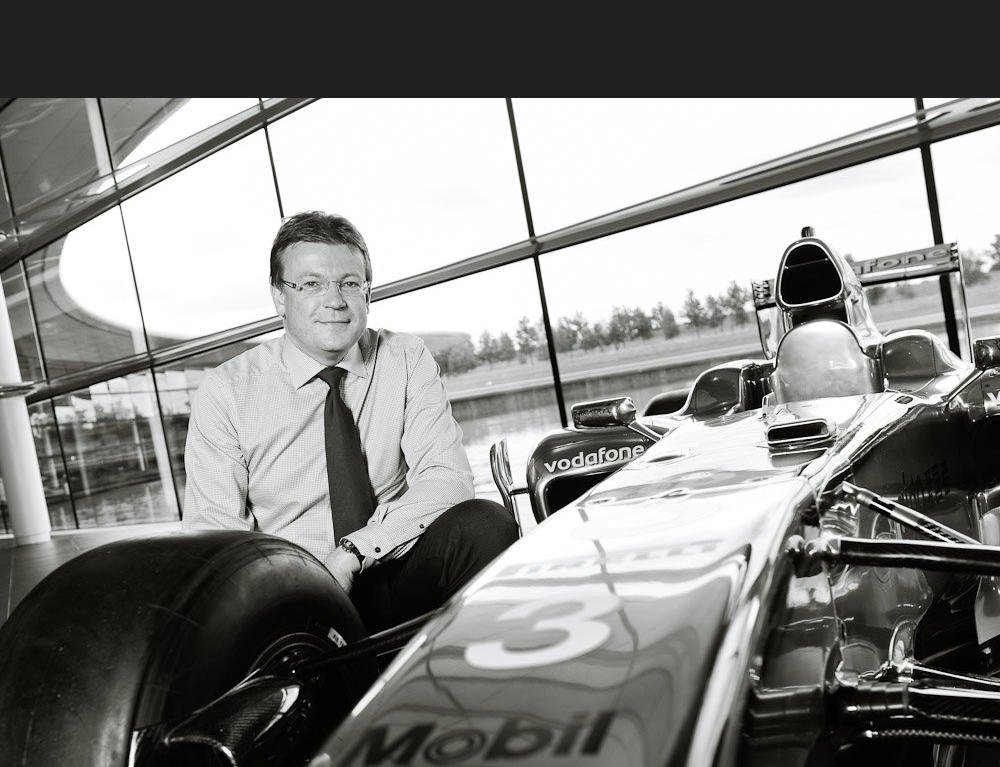 Black and white portrait photograph of Mclaren Finance Director with F1 car at Mclaren HQ